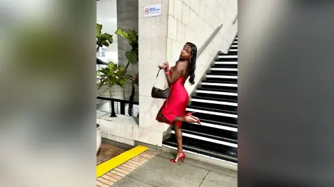 Elegant woman in a red cocktail dress holding a black handbag on modern indoor stairs.
