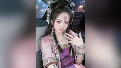 Young woman in ornate pink Hanfu traditional dress and silver headpiece sitting in a car at night.