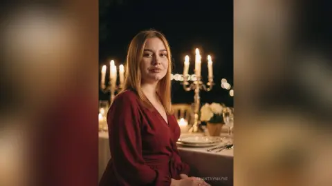 ShantayMayne poses in a red wrap dress next to a lit candelabra on a dining table.
