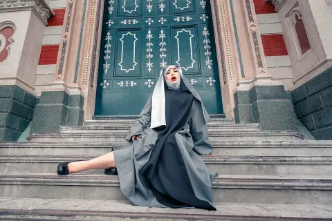 Moody portrait of a woman in a long grey and black dress sitting on stone stairs by a grand teal door.