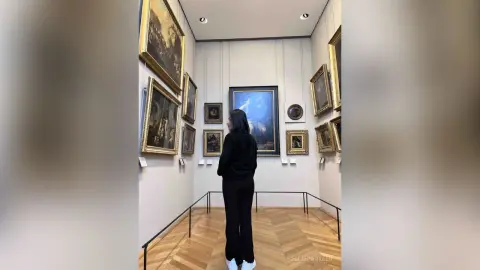 Woman in black outfit viewing classical oil paintings in a bright, modern art museum gallery.