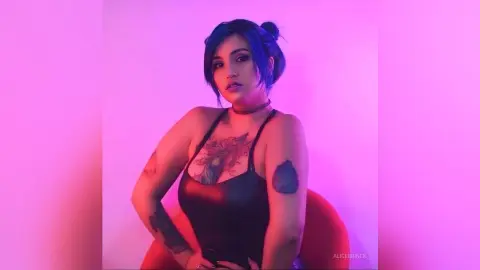 Tattooed woman in a black bodysuit posing under moody pink neon lighting.