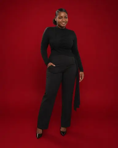 LilyReeds smiling in a tight black long-sleeve bodysuit and black pants against a red background.