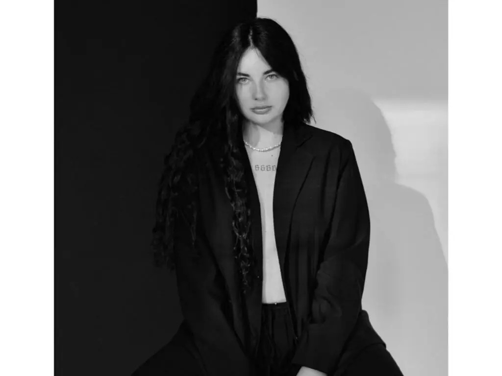Moody black and white portrait of a woman with long wavy hair wearing a black blazer and pearl necklace.