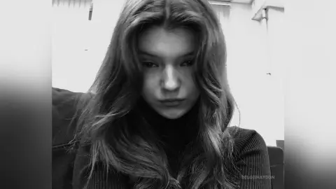Moody black and white portrait of a young woman with long wavy hair wearing a dark turtleneck sweater.