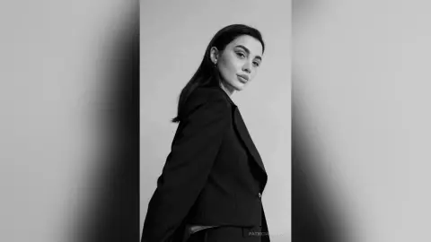 Elegant woman in a black blazer posing for a moody black and white studio portrait.