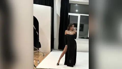 Elegant woman in a black off-the-shoulder evening gown posing in a minimalist photo studio.