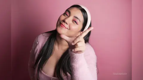 Smiling woman in a pink sweater and headband posing against a soft pink background.