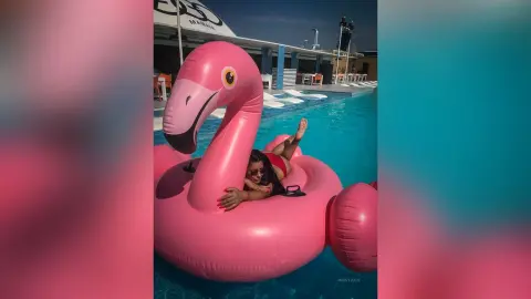 MissyJolie reclines in a pink flamingo floatie in a swimming pool wearing a red bikini.