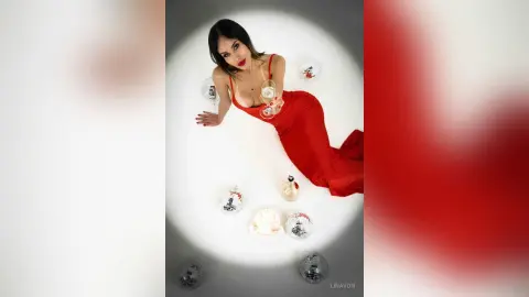 Glamorous woman in a red evening gown holding champagne amidst disco balls in a dreamy, festive setting.