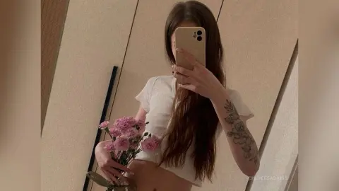 Young woman in a white t-shirt holding pink flowers for a soft, aesthetic mirror selfie.