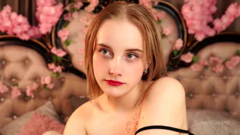 Blonde woman with red lipstick posing in a romantic bedroom setting decorated with pink cherry blossoms.