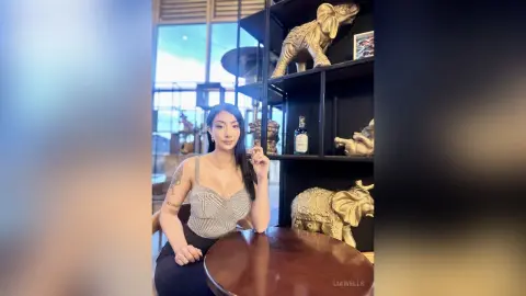 Elegant woman in a grey sparkly top sitting at a table in a modern lounge with gold elephant decor.