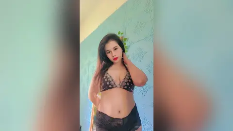 Young woman in a black sequined bikini top posing confidently against a light blue textured wall.