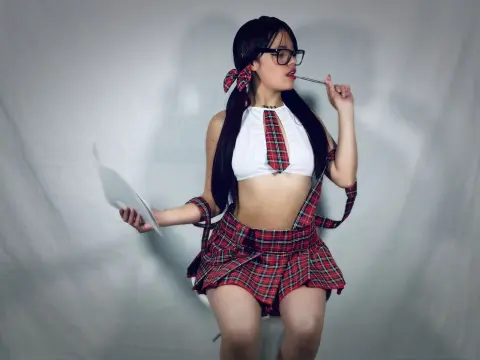 Young woman in a red plaid schoolgirl outfit and glasses holding a paper against a grey studio background.