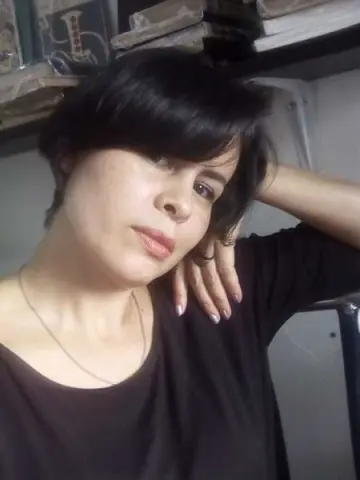 Woman with short dark hair wearing a black t-shirt and silver necklace in a cozy indoor setting.
