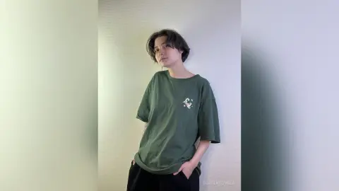 Young woman in an oversized dark green graphic t-shirt posing against a plain white wall with a relaxed mood.