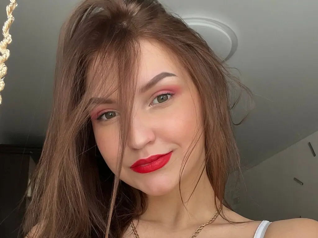 Young woman with long brown hair and red lipstick smiling in a bright indoor setting.
