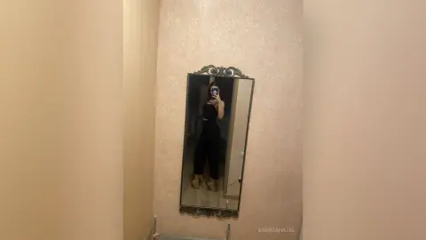 AndreaHazel poses for a mirror selfie wearing a black crop top and black leggings.