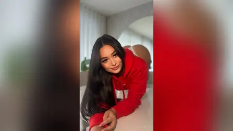Smiling young woman in a red hoodie relaxing in a bright, modern minimalist living room.