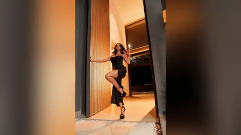 Elegant woman in a black slit dress posing in a modern luxury doorway at night.