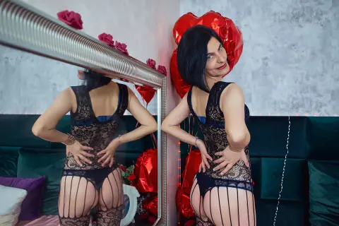 Woman in black lace lingerie posing in a bedroom with red heart balloons for a romantic mood.