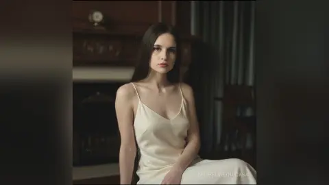 Elegant woman in a white silk slip dress sitting in a moody, dimly lit vintage interior.