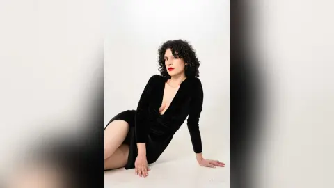 RoxyGraff poses in a black long-sleeved velvet dress with a deep v-neckline against a plain white background.