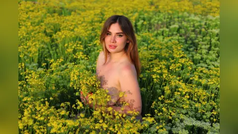 Young woman in a natural setting posing amidst a vibrant field of yellow wildflowers during golden hour.