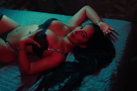 Sensual woman in black lace lingerie relaxing on a textured bed under moody teal lighting.