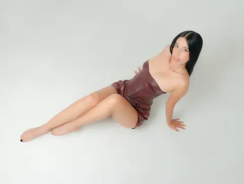 Young woman in a brown strapless dress sitting on a white floor in a minimalist studio setting.