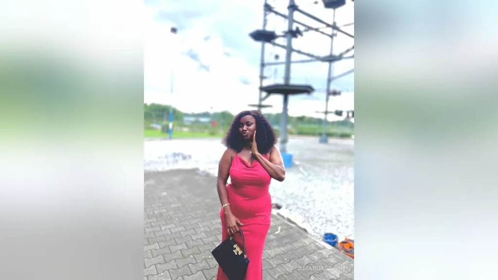 AmandaCaIvin — AmandaCaIvin stands outdoors in a tight red dress holding a black handbag.