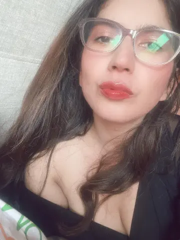 Zharid_Parker wearing glasses and red lipstick, posing in a black top with her long brown hair down.