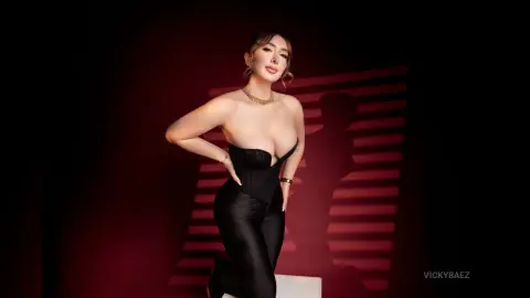 Glamorous woman in a black corset and satin pants posing against a dramatic red shadow background.
