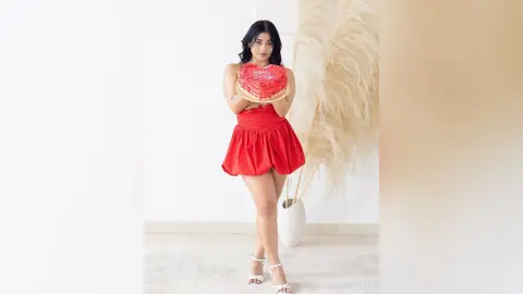 Young woman in a red mini dress holding a birthday cake in a bright, minimalist studio setting.