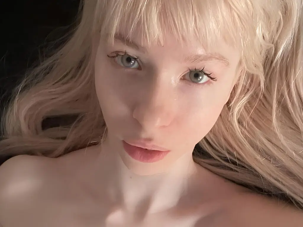 Close-up portrait of a blonde woman with bangs looking into the camera with a soft, dreamy expression.