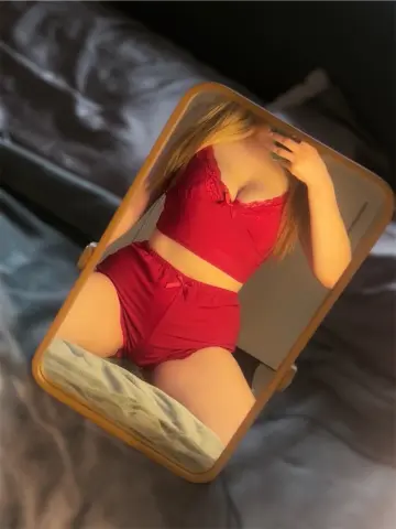 Young woman in red lace camisole and matching shorts relaxing in a cozy bedroom setting.