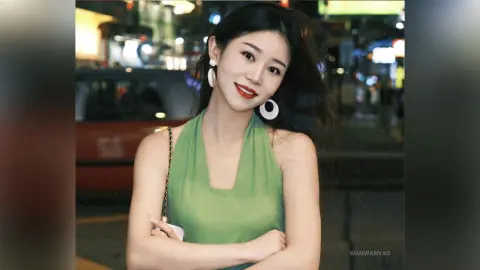 Smiling young woman in a green halter top posing outdoors at night in a city setting.