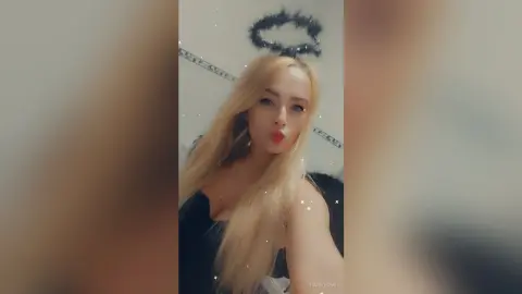 Blonde woman in a black outfit making a kissy face in a cozy indoor setting.