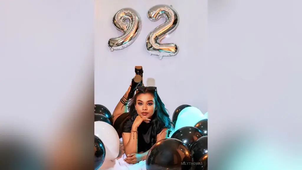 MilyThomas β Young woman in black outfit celebrating 92nd birthday with silver balloons in a festive indoor setting.