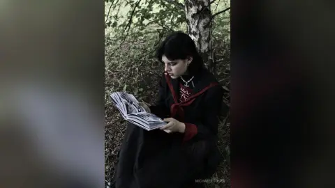 Young woman in a black vintage dress reading a book in a moody, shaded forest setting.