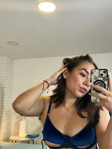 Young woman in a navy blue velvet bra taking a casual mirror selfie in a bright room.