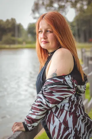 Redheaded woman in a zebra print jacket looking thoughtfully over a peaceful lake setting.