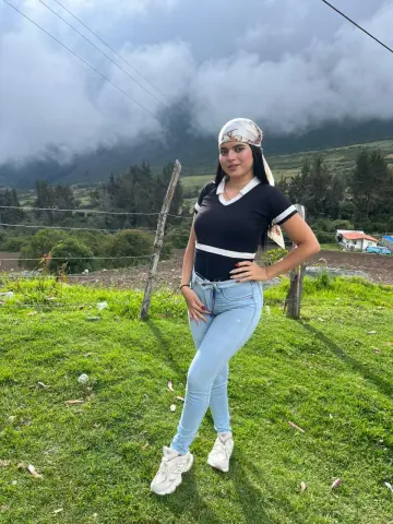 Smiling woman in a black v-neck shirt, light blue jeans, and headscarf posing in a misty mountain meadow.