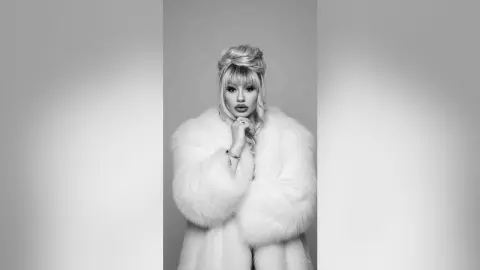 Glamorous woman in a white faux fur coat posing elegantly against a minimalist studio background.