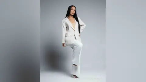 Elegant woman in a white oversized blazer and trousers posing against a minimalist grey studio background.
