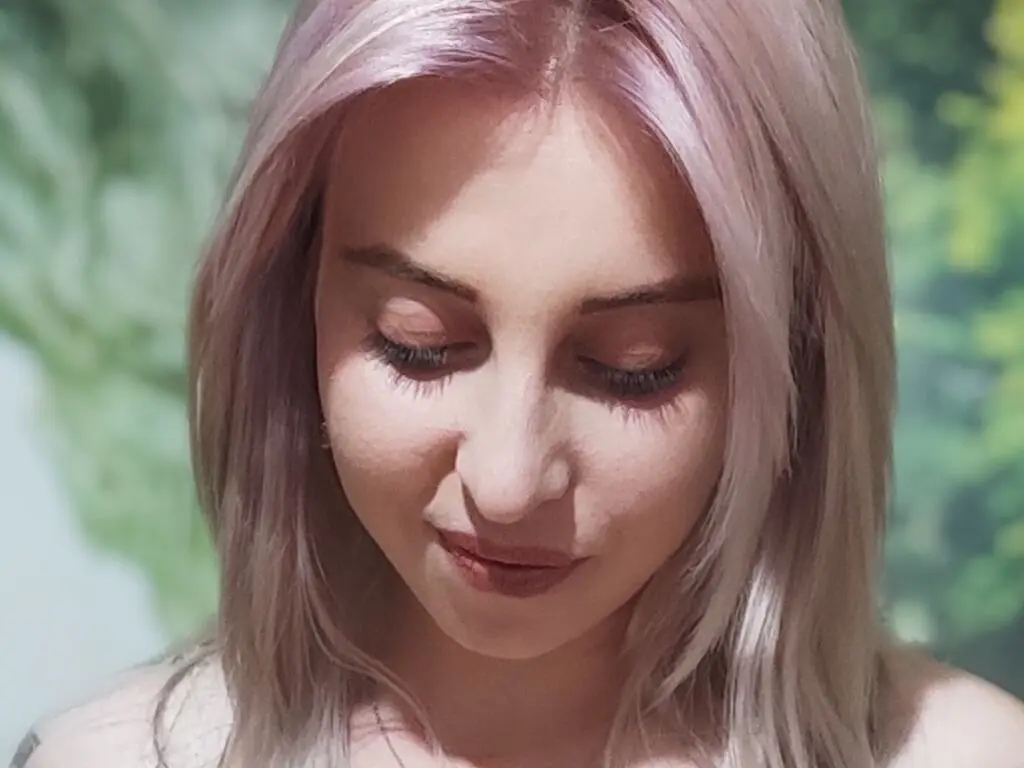 Serene woman with pastel pink hair looking down in a sunlit outdoor setting.