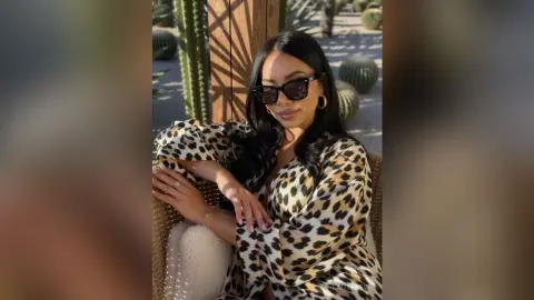 Stylish woman in leopard print blouse and sunglasses relaxing in a sunny desert garden setting.