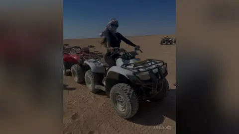 Adventurous woman in black activewear and face mask riding a grey ATV across a vast desert landscape.