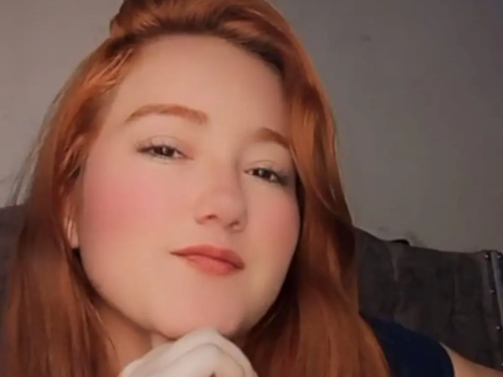 Redheaded woman with soft makeup smiling in a cozy indoor setting.